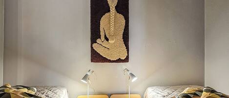 Habitación con dos camas, cada una con ropa de cama estampada, un tapiz colgado en la pared y lámparas de noche.