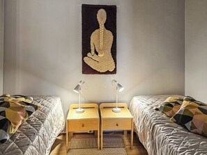 Une chambre avec deux lits, chacun agrémenté de draps à motifs, une tapisserie murale et des lampes de chevet.