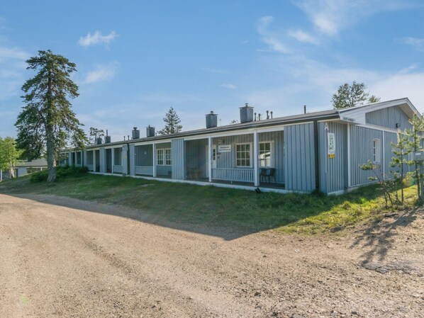 Une rangée de chalets de plain-pied, chacun doté d’une véranda, une allée en gravier et un grand arbre sur la gauche.