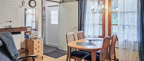 A dining area with a wooden table and chairs, a chandelier, and a view through a window with curtains.