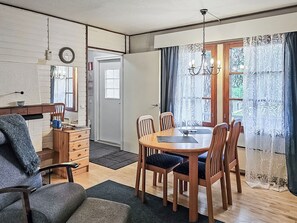 Un comedor con una mesa y sillas de madera, una araña y vistas a través de una ventana con cortinas.