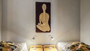 A room with two beds, each with a geometric-patterned duvet, a wooden nightstand with a lamp, and a tapestry depicting a seated figure on the wall. - Saariseläntie 8 a 8 by Interhome (Inari)