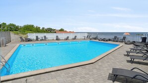Ein rechteckiger Swimmingpool mit klarem, blauem Wasser, umgeben von Liegestühlen und einer gepflasterten Liegefläche.