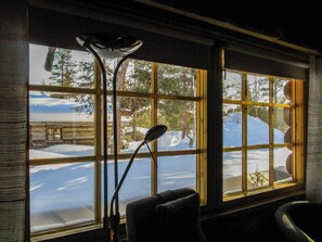 A room with a large window offering a view of a snowy landscape and a cabin.