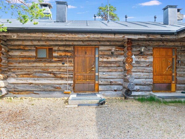 A log cabin with three wooden doors, a metal roof, and a gravel driveway.