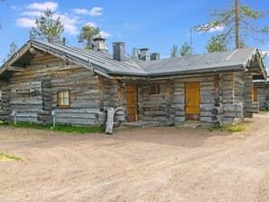 A log cabin with a metal roof, wooden doors, and a gravel driveway.