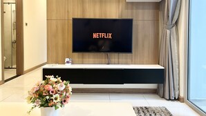 Un salon moderne avec un téléviseur fixé au mur affichant le logo « NETFLIX », un mur en bois, une console blanche, un vase de fleurs et une porte-fenêtre coulissante.
