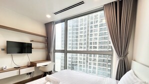Une chambre d’hôtel comprenant un lit, un téléviseur fixé au mur, un bureau avec une chaise et une grande fenêtre donnant sur la ville.