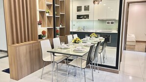 Un espace repas moderne avec une table en verre, des chaises blanches et une cloison en bois dotée d’étagères.