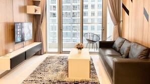 Un salon moderne doté d’un téléviseur à écran plat, d’un canapé, d’une table basse et offrant une vue sur un immeuble d’habitation grâce à de grandes fenêtres.