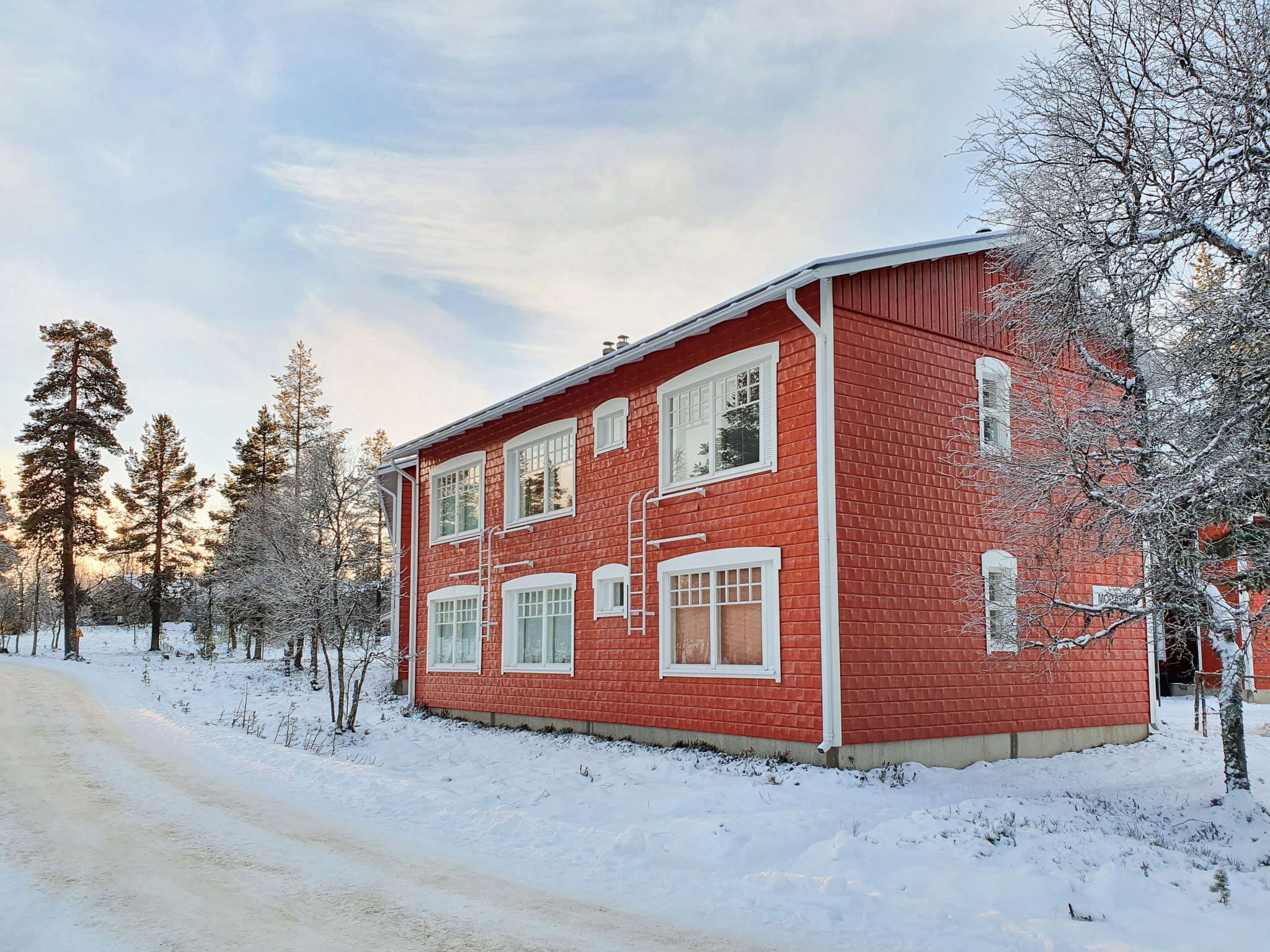 Un bâtiment rouge en briques, à deux étages, doté de nombreuses fenêtres, et un paysage enneigé.
