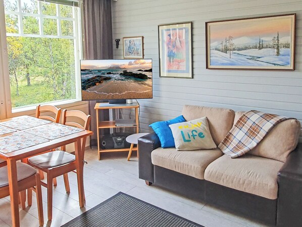 Un salon comprenant un canapé, un téléviseur, une table à manger avec des chaises et des œuvres d’art accrochées au mur.