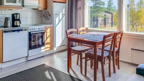 Una cocina con armarios de madera, microondas, cafetera y mesa de comedor con sillas.