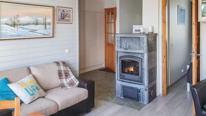 Una sala de estar acogedora con chimenea, un sofá con una manta de cuadros y un cuadro de un paisaje nevado.