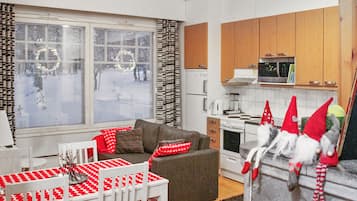 A cozy living room with a sofa, a dining table with a red and white tablecloth, and a kitchen area with wooden cabinets and a stove.