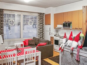 A cozy living room with a sofa, a dining table with a red and white tablecloth, and a kitchen area with wooden cabinets and a stove.