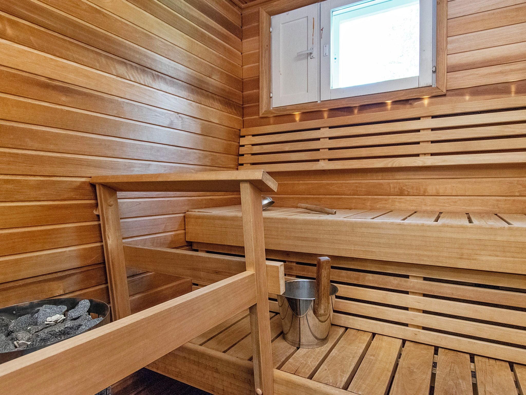 A sauna with wooden benches, a window, and a metal bucket.