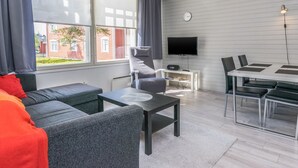 A modern living room with a sofa, a coffee table, a TV, and a dining area with chairs and a table.