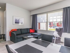 En moderne stue med en grå sofa, et spisebord og udsigt til en rød bygning gennem vinduet.