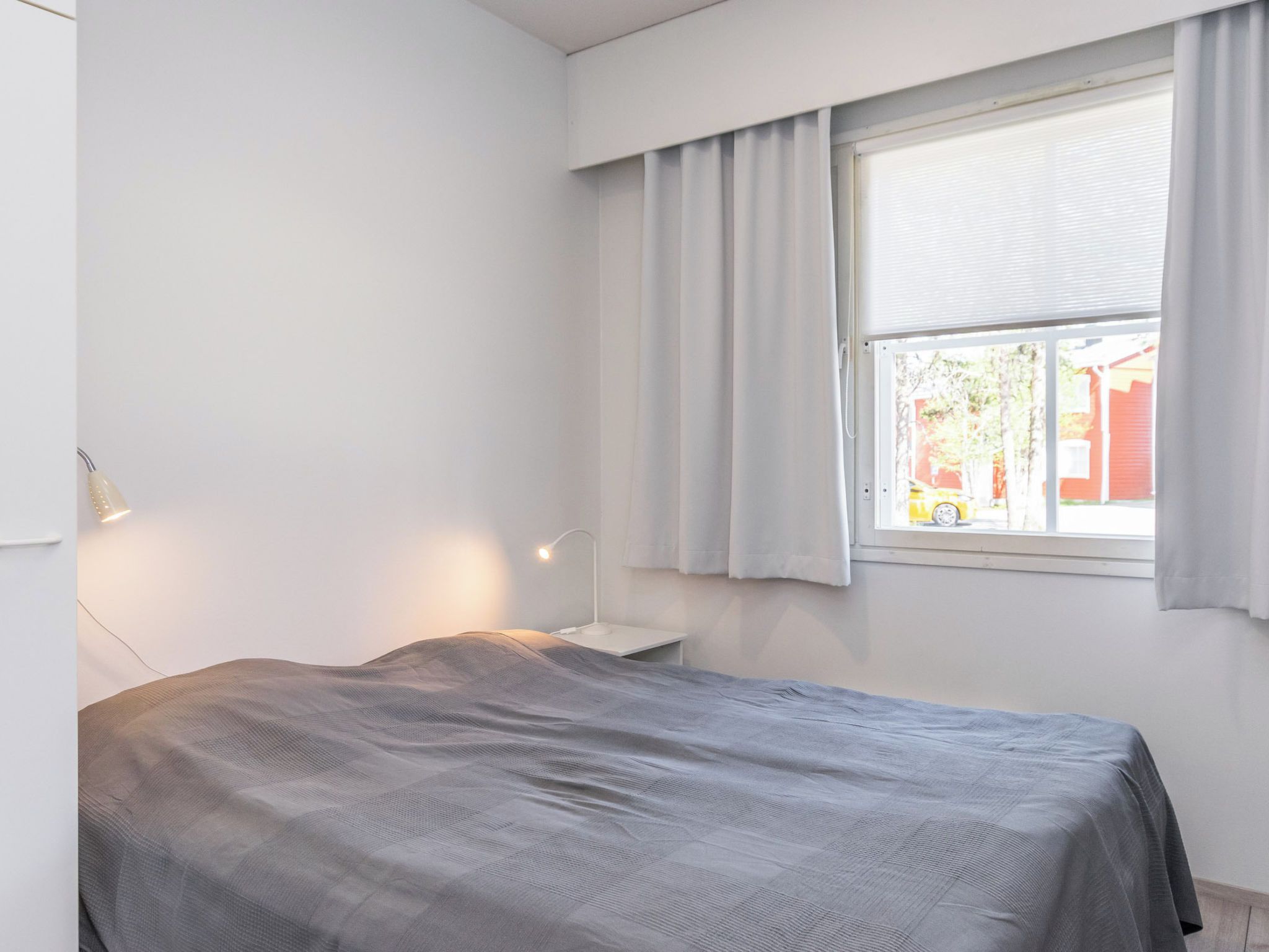Un dormitorio con cama, mesita de noche, lámpara y ventana con cortinas.