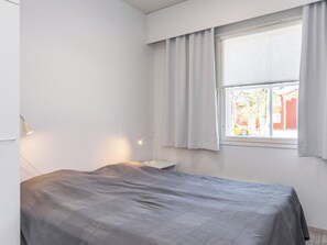 A bedroom with a bed, a bedside table, a lamp, and a window with curtains.