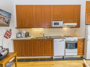 Een compacte keuken met houten kastjes, een magnetron, een Bosch vaatwasser, een fornuis en een spoelbak.