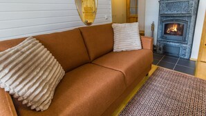 Een gezellige woonkamer met een bruine bank, een open haard en een vloerkleed met een patroon.