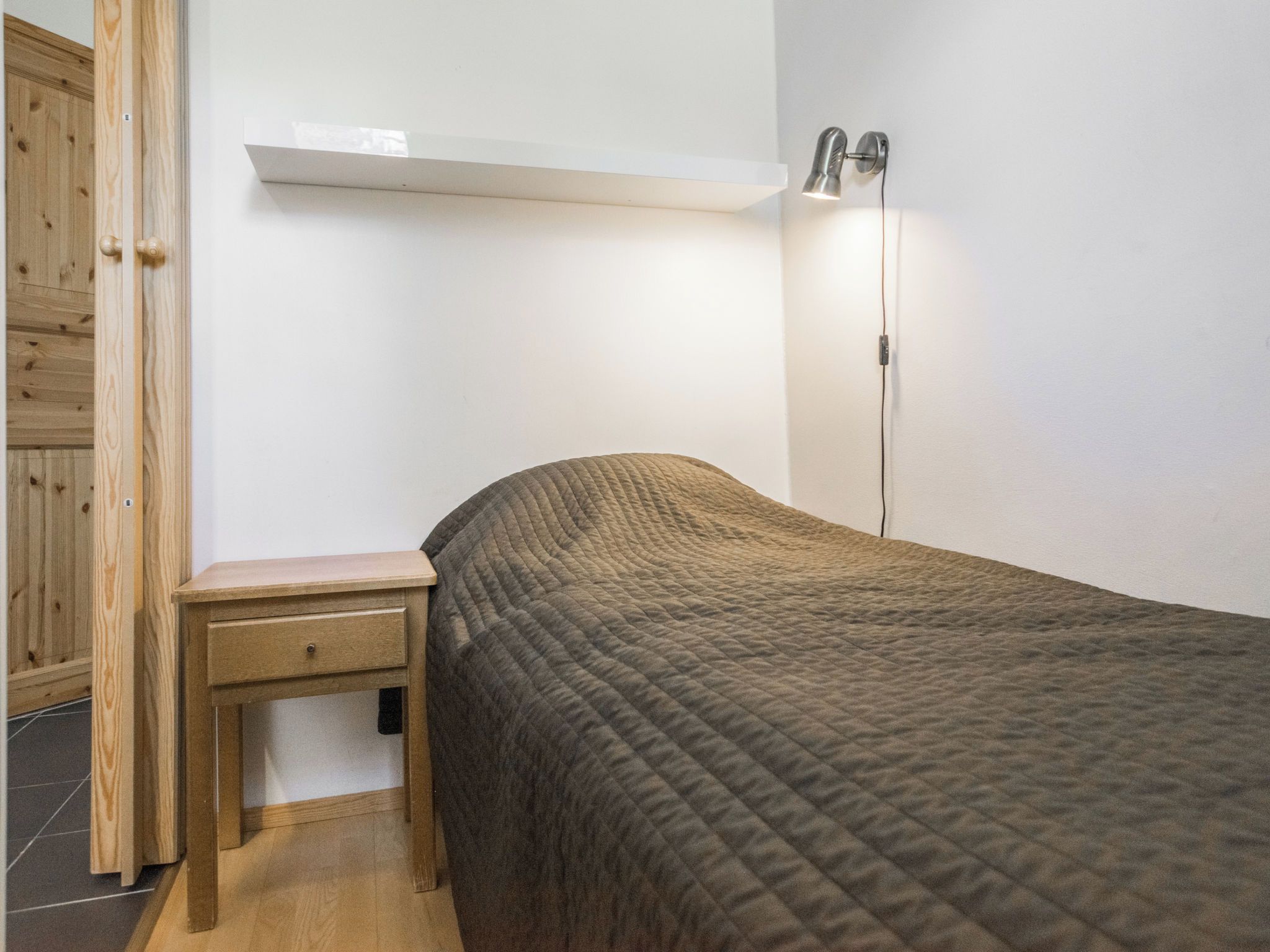 Une chambre à coucher comprenant un lit, une table de chevet, une étagère murale et une lampe sur pied.