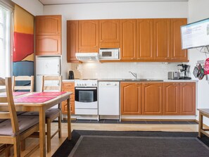 Cocina compacta con armarios de madera, microondas, estufa y lavavajillas.