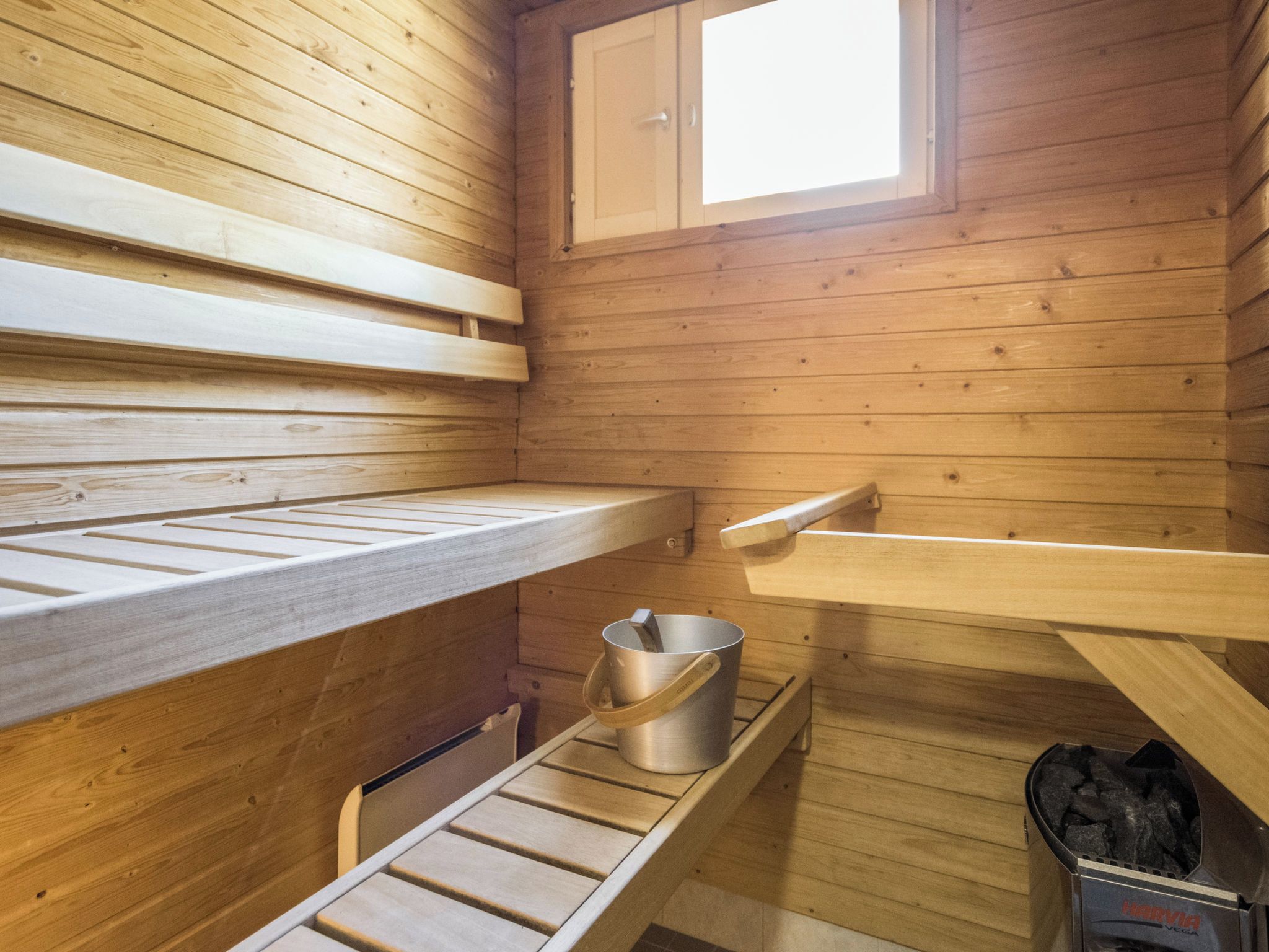 Een sauna met houten banken, een metalen emmer en een sauna-oven.