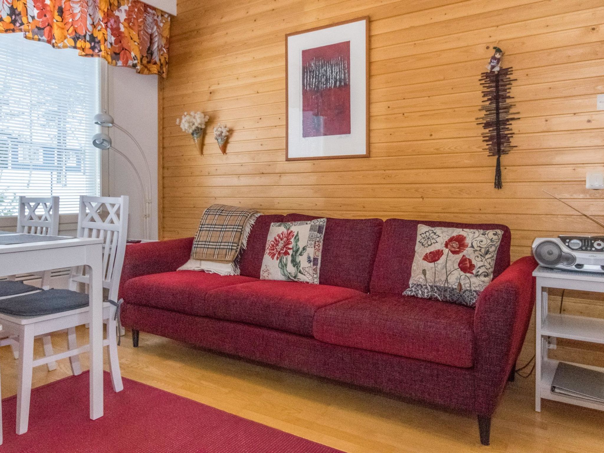 A cozy room with a red sofa, white chairs, a wooden floor, and a wooden wall.