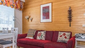 A cozy room with a red sofa, white chairs, a wooden floor, and a wooden wall.