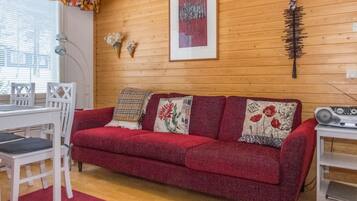 A cozy room with a red sofa, white chairs, a wooden floor, and a wooden wall.