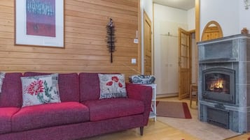 Een woonkamer met een rode bank, een open haard en een houten wand.
