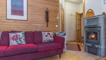 A cozy living room with a red sofa, a fireplace, and a wooden wall.