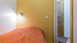 A bedroom with a bed, a wall socket, and a door leading to another room.