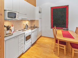 A compact kitchen with white cabinets, a microwave, a stove, and a sink. There's a dining table with chairs and a red placemat. - Apartment helmi saariselkä by Interhome (Inari)