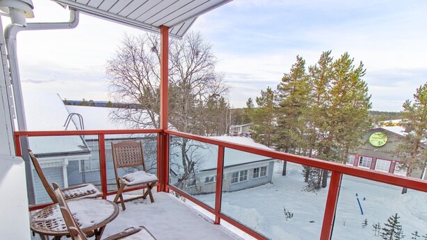 A balcony with a view of a snowy landscape, a chair, and a table covered in snow.
