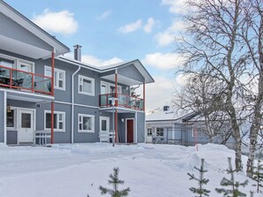 A multi-story residential building with a balcony, a covered porch, and a snow-covered ground. - Apartment helmi saariselkä by Interhome (Inari)