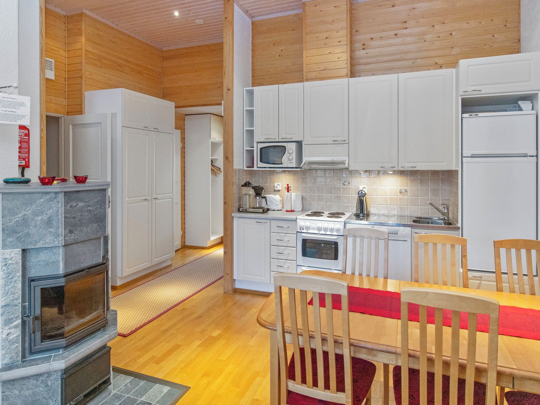 Una cocina moderna con armarios blancos, microondas integrado, estufa y comedor con sillas de madera y camino de mesa rojo.