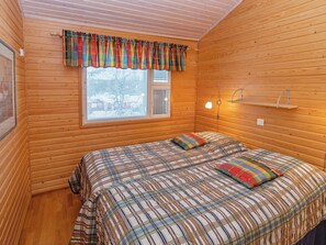 A wooden cabin room with a bed, a window with blinds, and a wall-mounted shelf.