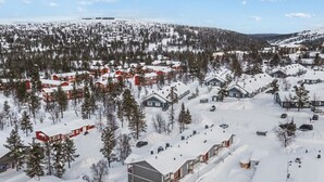 A snow-covered residential area with houses and buildings, surrounded by trees and a hilly landscape.