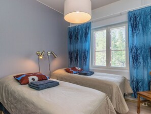 Une chambre avec deux lits, une fenêtre avec des stores et une lampe suspendue.