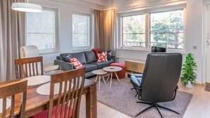 Ein modernes Wohnzimmer mit einer Couch, einem Esstisch, Stühlen und einem großen Fenster mit Jalousien.