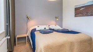 Ein Schlafzimmer mit Bett, Nachttischlampen, einem Nachttisch, einem Fenster mit Vorhängen und einem Wandbild.