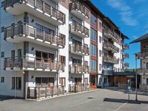 Un edificio residencial de varios pisos con balcones, un estacionamiento y un cielo despejado.