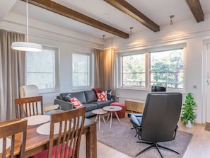 Una sala moderna con sofá, sillones, una mesa de comedor y ventanas amplias.