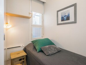 A small, neatly arranged bedroom with a bed, a bedside table, a lamp, and a framed picture on the wall.