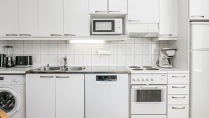 Una cocina moderna con armarios blancos, microondas, cafetera, lavavajillas y lavadora.