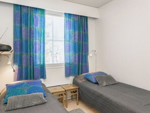 A small, tidy room with two single beds, a small table, and a window with patterned curtains.